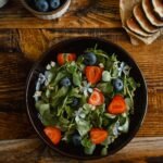 Top view of a fresh salad with strawberries, blueberries, and flowers on a rustic table.